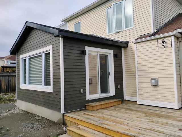 Completed rear home addition with grey siding and a timber deck